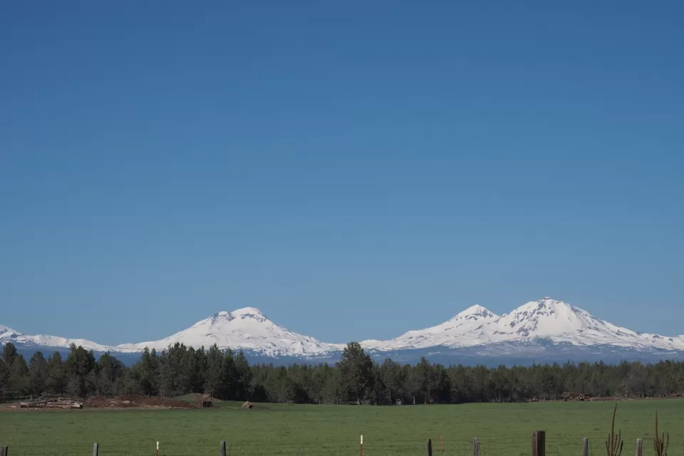 The Three Sisters, snow-covered mountains in Central Oregon, are visible in the distance beyond a farm.